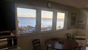 Un coin repas avec vue sur la mer, une horloge au mur et un four à micro-ondes sur le plan de travail.