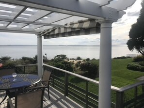 A covered outdoor seating area with a table and chairs, overlooking a body of water and a grassy landscape. - Spectacular views from our comfortable beachfront home!! (Waterford)