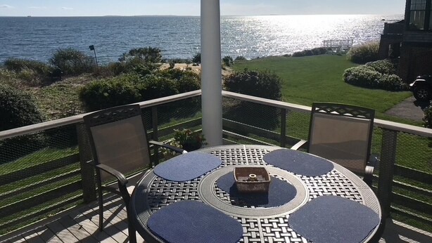 Une terrasse couverte, dotée d’une table et de chaises, qui offre une vue sur une plage et l’océan.