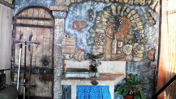 A rustic room with a wooden door, a stone wall mural, and a small table with a plant. - Hostal La Pianista TRINIDAD (Trinidad)