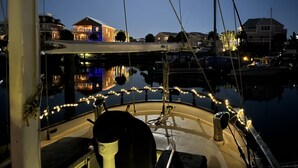 A boat docked at a marina with houses in the background and string lights on the bow.