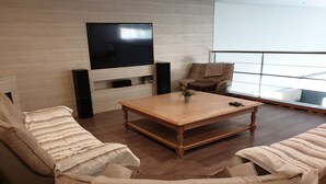 A modern living room with a flat-screen TV mounted on a light-colored wall, a wooden coffee table, and two beige sofas with striped cushions. - Lovely loft with private pool (Le Creusot)