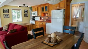 Une cuisine compacte avec des meubles en bois, un réfrigérateur blanc et un coin repas comprenant une table et des chaises en bois.