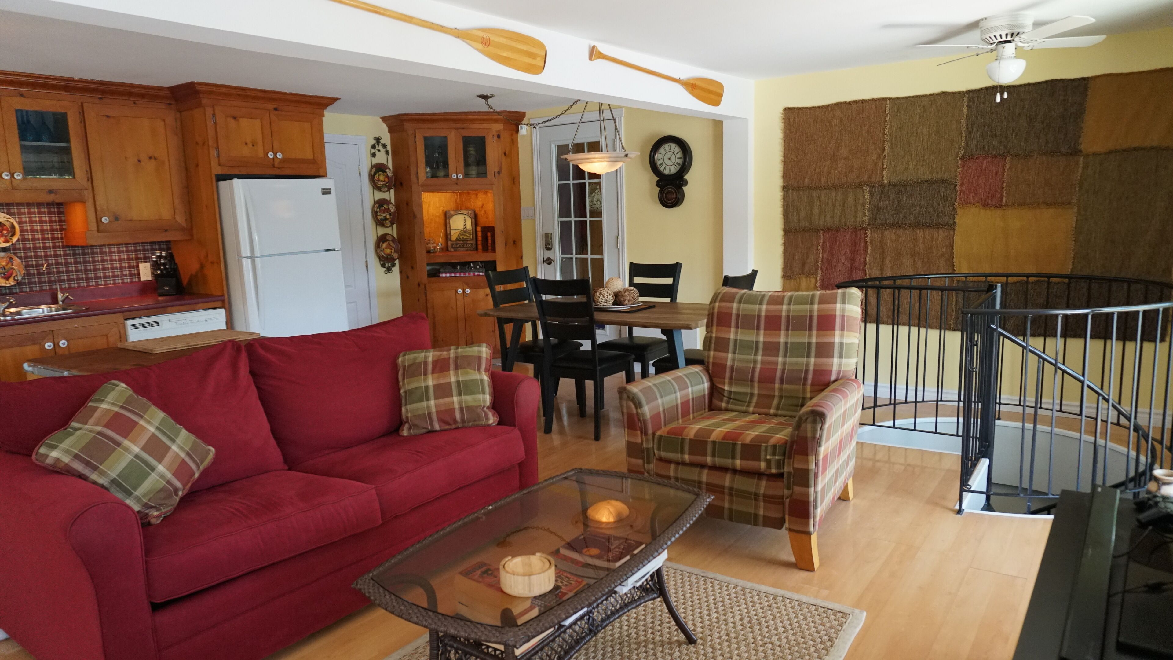 Una sala de estar con un sofá rojo, sillones escoceses, una mesa de centro de vidrio y una zona de comedor con una mesa y sillas de madera.