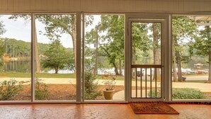 Ett rum med en stor skjutdörr i glas som leder ut till en vacker utsikt över en sjö, omgiven av träd och en parkeringsplats.