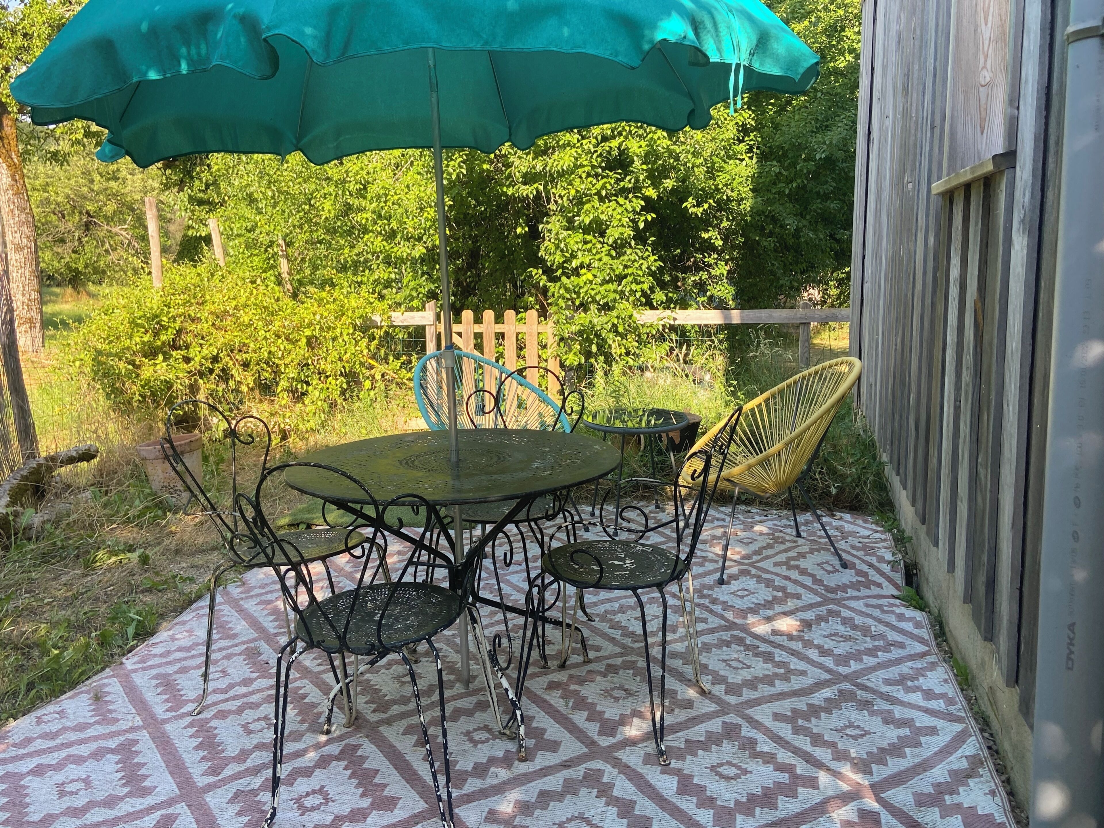 Un patio al aire libre con una mesa, sillas, un paraguas verde y un suelo estampado.