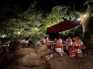 An outdoor dining area with tables and chairs, surrounded by trees and under a large umbrella.