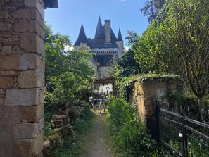 A stone pathway leading to a castle-like structure with multiple towers, surrounded by lush greenery and a metal fence. - “Perfectly situated” for Lascaux/Grottes, River Châteaux canoë shade fly screens (Valojoulx)