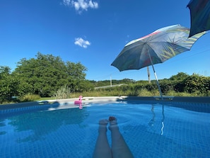 A swimming pool with clear blue water, a pink flamingo float, and a large umbrella providing shade.