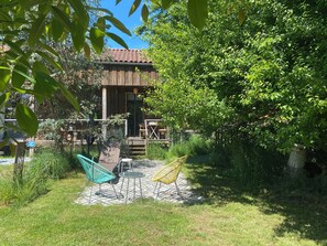Un bâtiment en bois, doté d’un toit en tuiles, entouré d’une végétation luxuriante et agrémenté d’un patio avec des meubles d’extérieur.