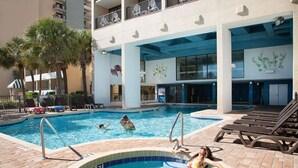 A swimming pool area with lounge chairs, palm trees, and a building with balconies. - Breakers Tower 1BR Oceanfront Condo (Myrtle Beach)