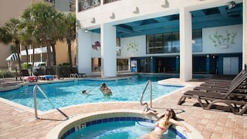 A swimming pool area with lounge chairs, palm trees, and a building with balconies.
