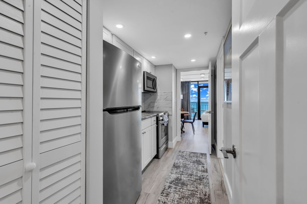 A modern kitchen with stainless steel appliances, a dining area with a view, and a hallway leading to a balcony.