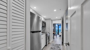 A modern kitchen with stainless steel appliances, a dining area with a view, and a hallway leading to a balcony. - Breakers Tower 1BR Oceanfront Condo (Myrtle Beach)