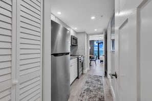 A modern kitchen with stainless steel appliances, a dining area with a view, and a hallway leading to a balcony.