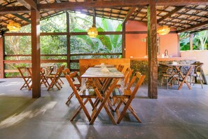 A restaurant with wooden tables and chairs, large windows with a view of greenery, and a stone wall.