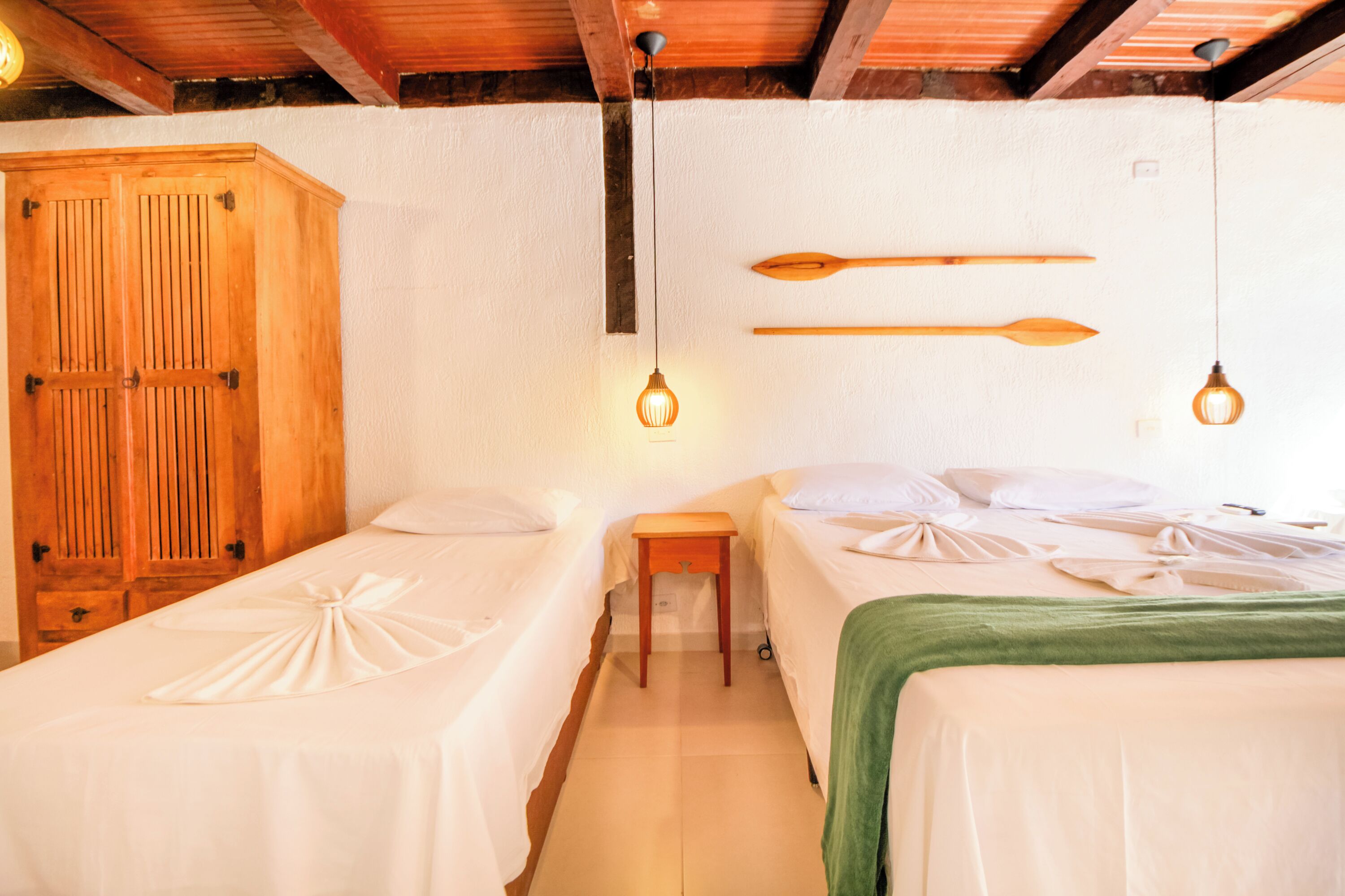 A room with two beds, wooden wardrobe, and two pendant lights.