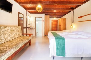 Una habitación de hotel con techo de madera, una cama con manta verde, un sofá estampado con motivos florales, una puerta de madera y un televisor montado en la pared.