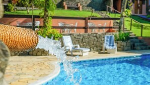 A pool with clear blue water, surrounded by stone tiles and a stone wall. There are lounge chairs and a small grassy area in the background. - VELINN Pousada Canoa Ilhabela (Ilhabela)