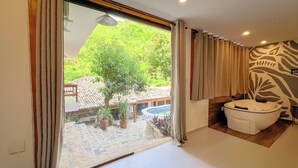 A bathroom with a bathtub, a large window with curtains, and a view of a pool and greenery outside. - VELINN Pousada Canoa Ilhabela (Ilhabela)