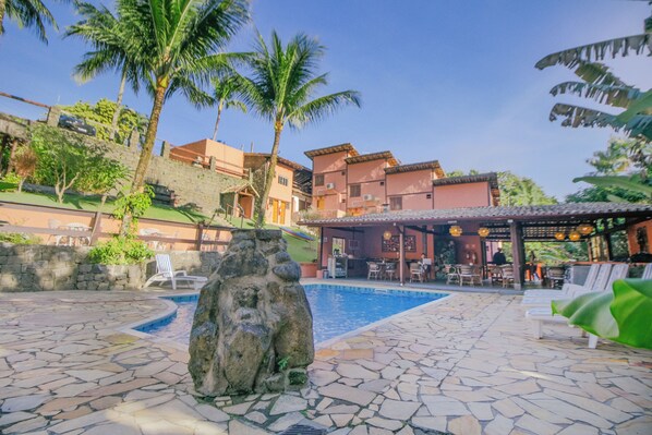 A pool area with stone flooring, lounge chairs, and a bar area with outdoor seating.