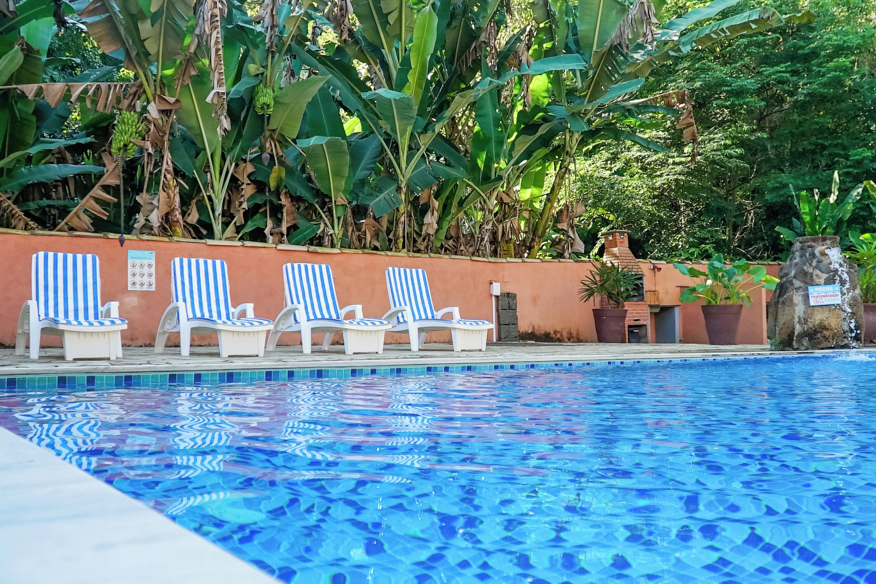 A swimming pool with blue tiles, surrounded by white lounge chairs with blue stripes, and a wall with a sign.