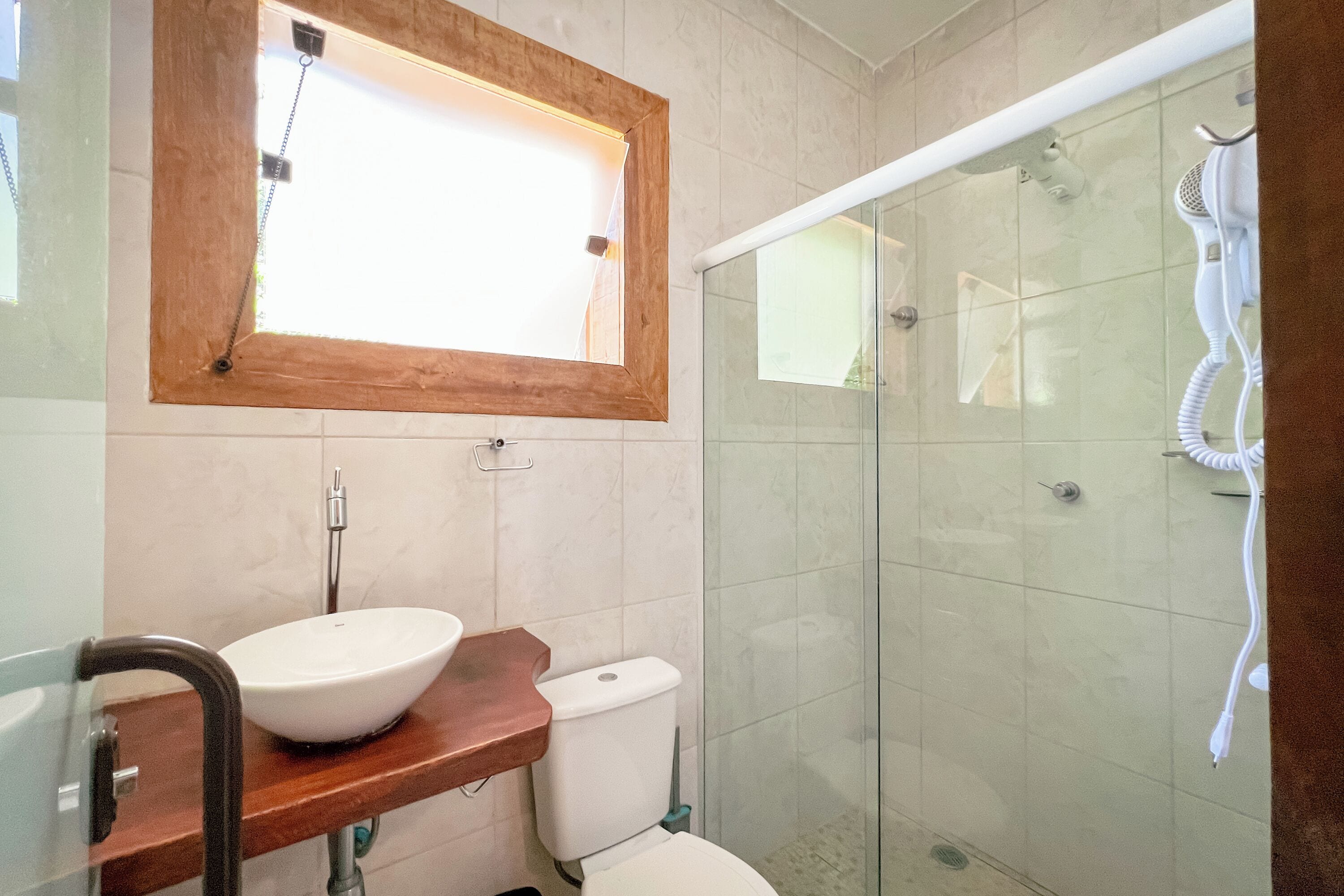 A bathroom with a wooden vanity, a white sink, a toilet, and a glass shower enclosure.