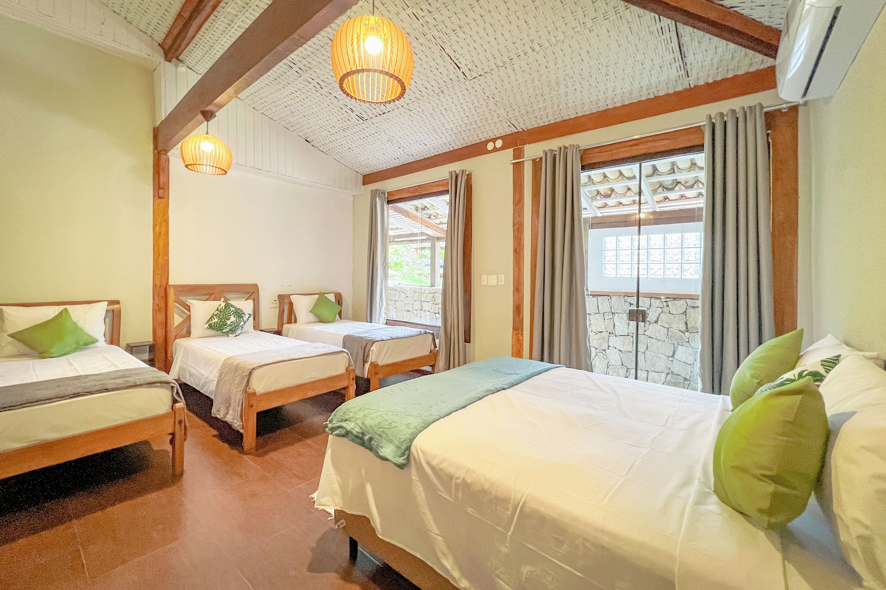Habitación de hotel con tres camas, vigas de madera, una lámpara de techo tejida y una pared de piedra.