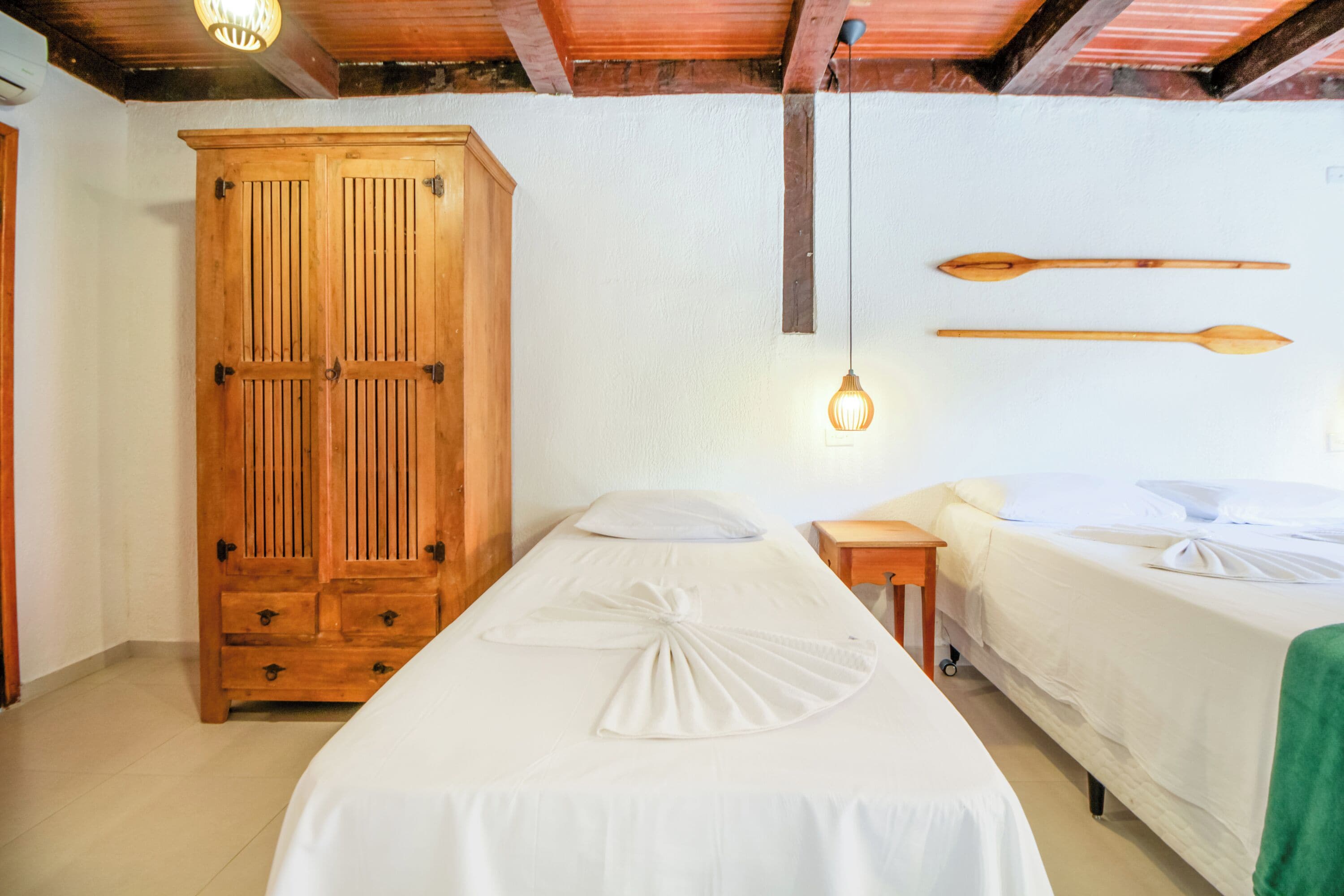Een kamer met een houten garderobe, twee bedden, een hanglamp en een houten decoratie aan de muur.