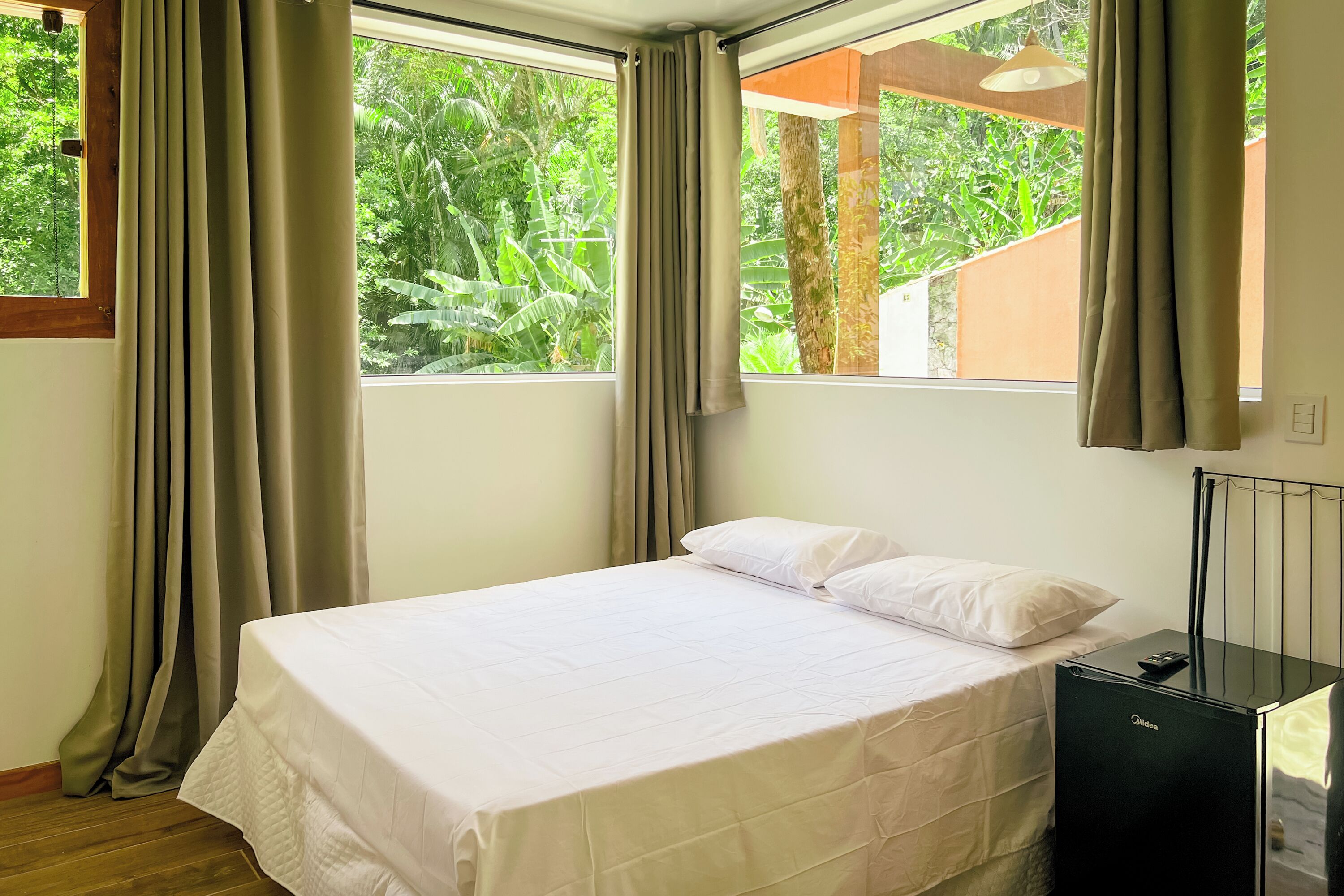 A bedroom with a bed, curtains, a window, and a black minibar.