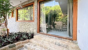 A stone exterior with a wooden window frame, a glass door, and a small stone staircase leading to a covered outdoor area. - VELINN Pousada Canoa Ilhabela (Ilhabela)