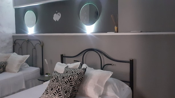 A bedroom with a bed, two bedside tables, and a wall-mounted shelf with decorative items. - Hostal Rodolfo y Nancy TRINIDAD (Trinidad)