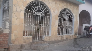 A building with three arched windows with metal bars, a brick wall, and a motorcycle parked outside. - Hostal Rodolfo y Nancy TRINIDAD (Trinidad)