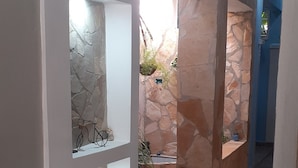 A corridor with stone walls and tiled flooring, leading to a room with a blue accent wall and a stone column. - Hostal Rodolfo y Nancy TRINIDAD (Trinidad)