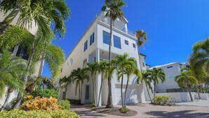 A modern two-story building with a white facade, surrounded by palm trees and a paved courtyard. - Luxury Townhome with a Rooftop Deck! - Changing Channels (Siesta Key)