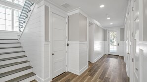 Un pasillo con paneles blancos, una escalera de madera y vistas al exterior.