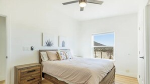 Une chambre à coucher avec un lit, une table de chevet en bois, un ventilateur de plafond et une fenêtre donnant sur un paysage désertique.