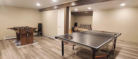 Una habitación con mesa de ping pong, mesa de futbolín y un sofá.