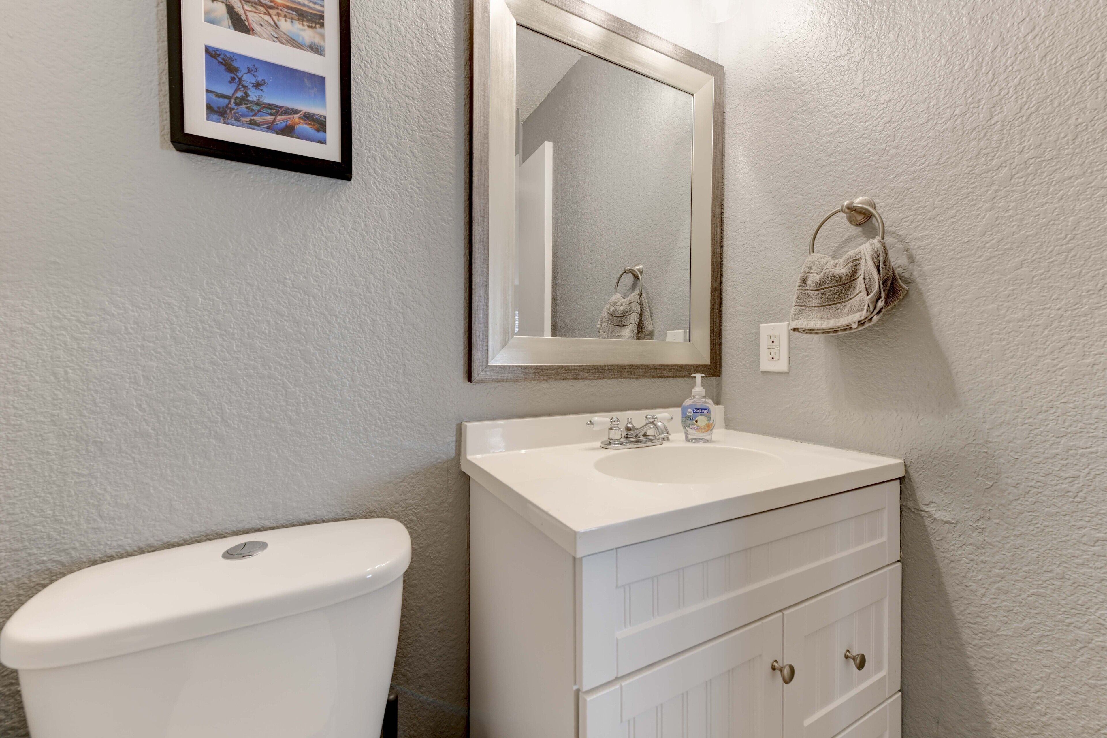 A bathroom with a white toilet, a white sink with a mirror above it, and a towel hanging on the wall.