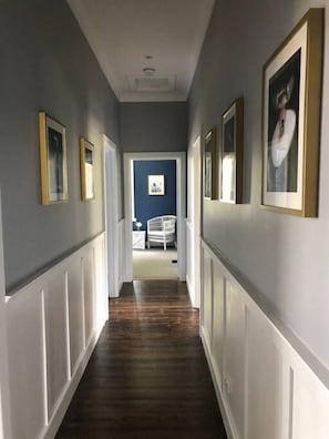 A hallway with framed pictures on the walls, a white door at the end, and a blue wall in the background.