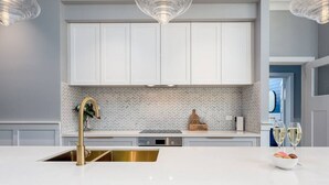 Una cocina moderna con armarios blancos, un grifo dorado y un respuesto de azulejos tipo espiga.