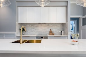 A modern kitchen with white cabinetry, a gold faucet, and a herringbone tile backsplash.
