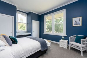 A bedroom with a large bed, two windows, a white nightstand, a wicker chair, and a framed picture on the wall. - Luxury Villa With Gorgeous Views, We Sleep 11 (Marysville)