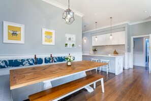 Une cuisine moderne avec des meubles blancs, une table à manger en bois et des luminaires suspendus.