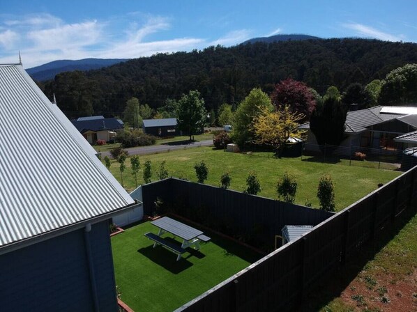 A residential area with a fenced backyard, a picnic table, and a view of a forested mountain range.