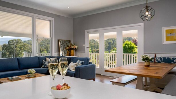 Una sala moderna con un sofá azul, una mesa de comedor con un cuenco de aperitivos y dos copas de vino blanco.