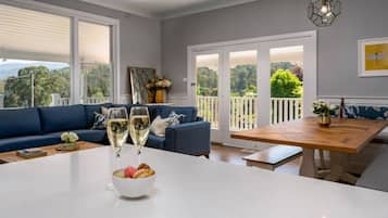 A modern living room with a blue sofa, a dining table with a bowl of snacks, and two glasses of white wine.