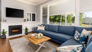 Una sala de estar con chimenea, un sofá azul y un ventanal con vistas a árboles.