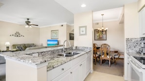 A compact kitchen with a central island, white cabinetry, and a dining area with wooden chairs. - Golf Membership Available! 2 BR/2BA, Pickleball, Pools, Near Gulf Beaches (Naples)