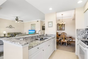 A compact kitchen with a central island, white cabinetry, and a dining area with wooden chairs.